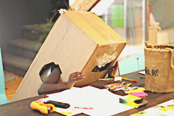 child playing with cardboard box and craft supplies