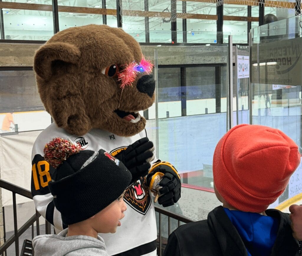 a bear mascot wearing a hockey jersey talking to kids wearing winter hats